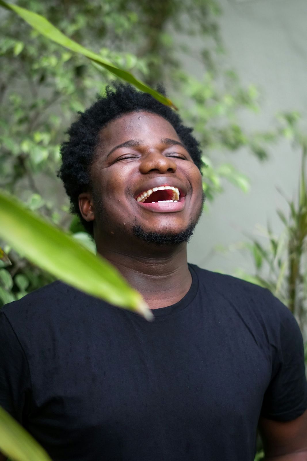 A young man laughing outdoors among green plants